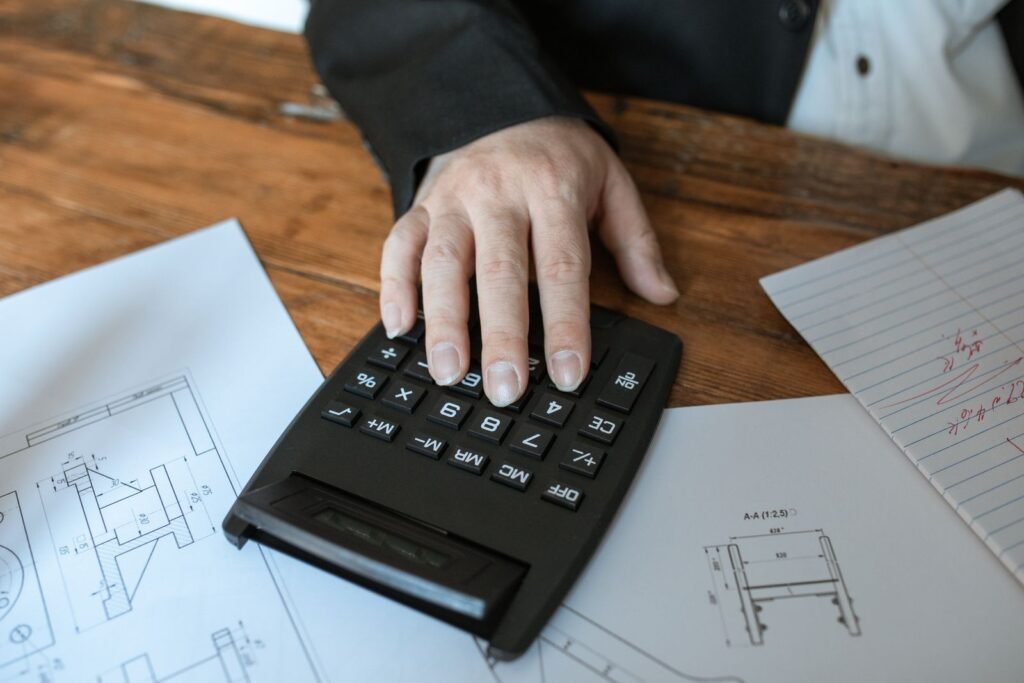 Mano usando una calculadora sobre planos arquitectónicos para calcular el valor de una propiedad
