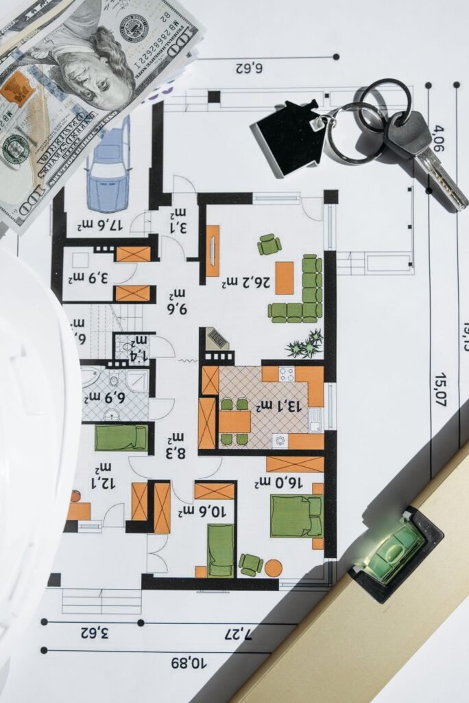 Plano arquitectónico de una vivienda con billetes de dólar y llaves apoyados encima